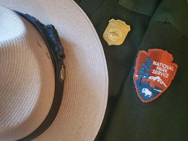This is a straw flat hat, green sweater with NPS arrowhead and NPS badge.