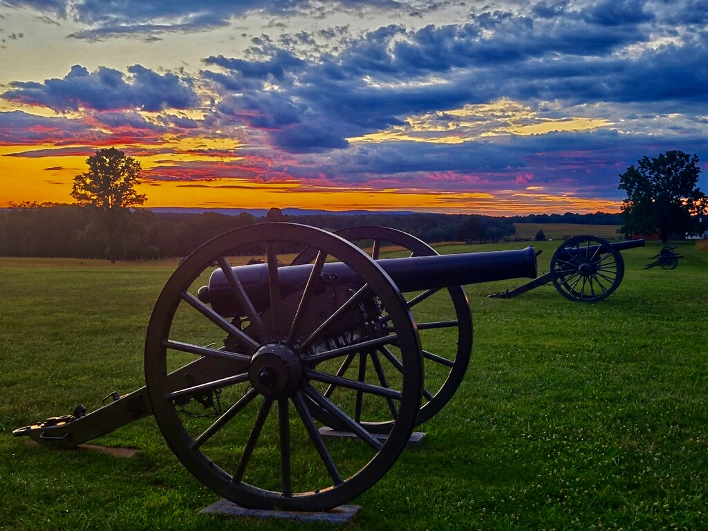 An orange, pink, and blue sunset sky behind a silhouetted cannon.