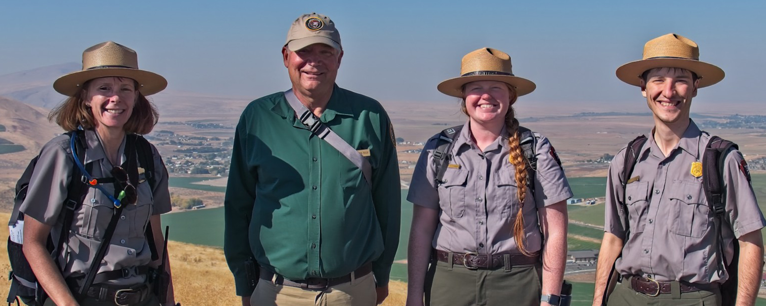 Two women and one man in a flat hat pose with another man in a green shirt. All are smiling.