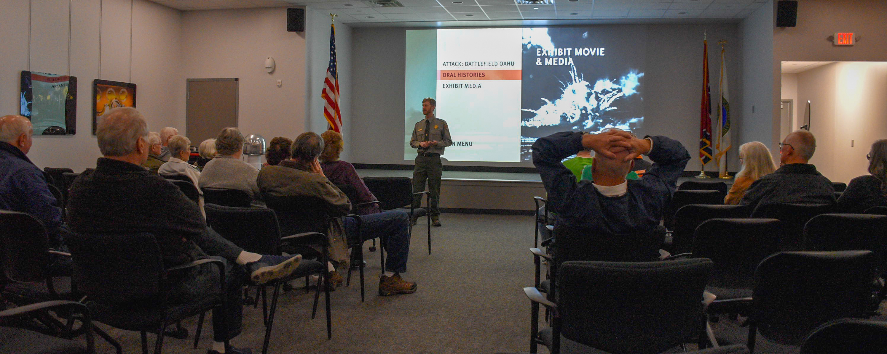 Ranger standing in front of a screen addressing a room full of people sitting in chairs.