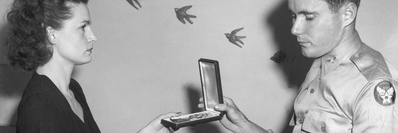 A women looks solemnly at a man who is handing her a medal.