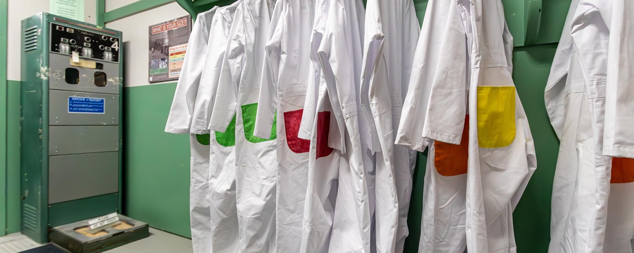 Several white lab coats with green, red, and yellow patches hang on a wall.