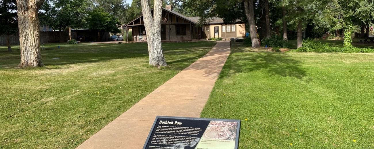 A wayside exhibit along a walkway leading to a small house.