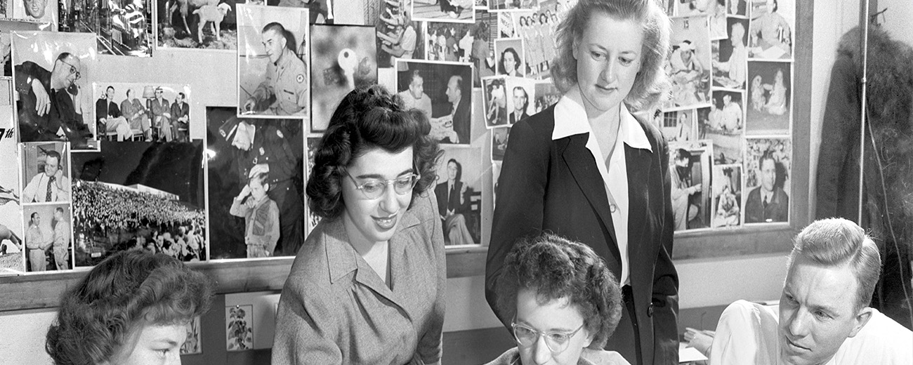 Black and white photo of a group of people with their backs to a wall full of photos.