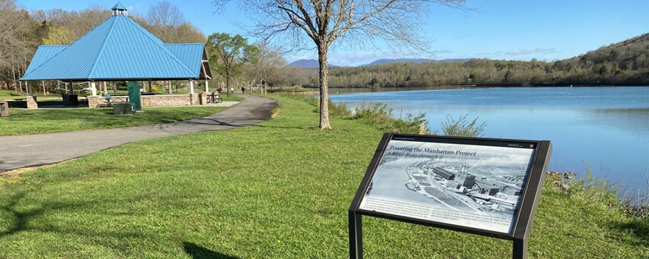 A wayside exhibit along a riverbank with a walking trail behind it.