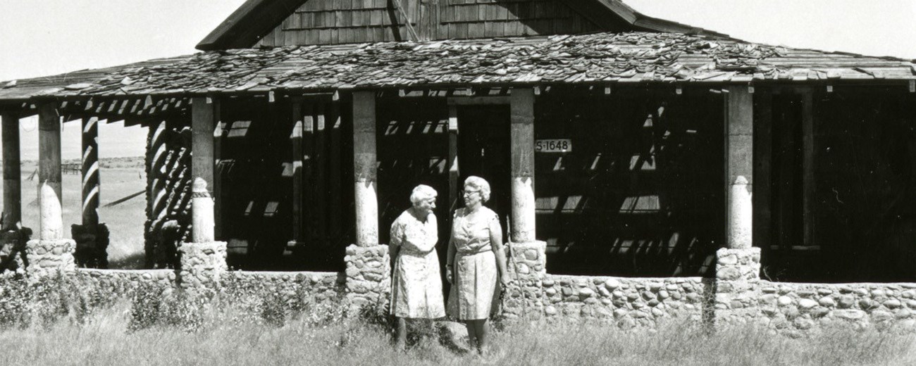 Black and white photo of two elderly women in front of an old, vacant house.