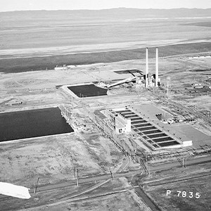 A black and white aerial photo of a 25 million gallon clear well for storage of cooling water (left), a filter plant in the lower center, and a coal fired steam plant in the upper center of photo.
