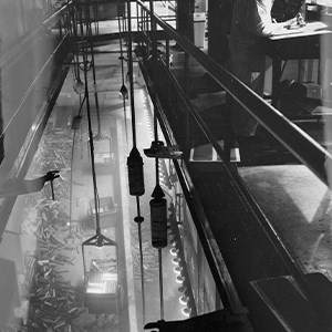 A black and white elevated photo of a narrow gap between two walls. Pipes run a long distance along the right-hand wall.