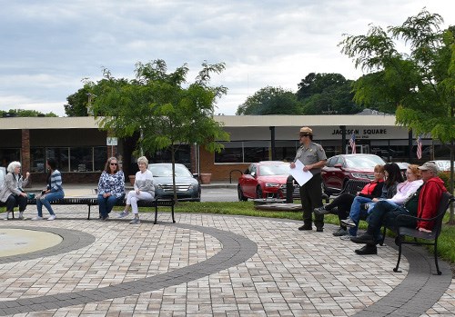 A group of people sitting on benches in a circular formation with a ranger speaking in the middle.