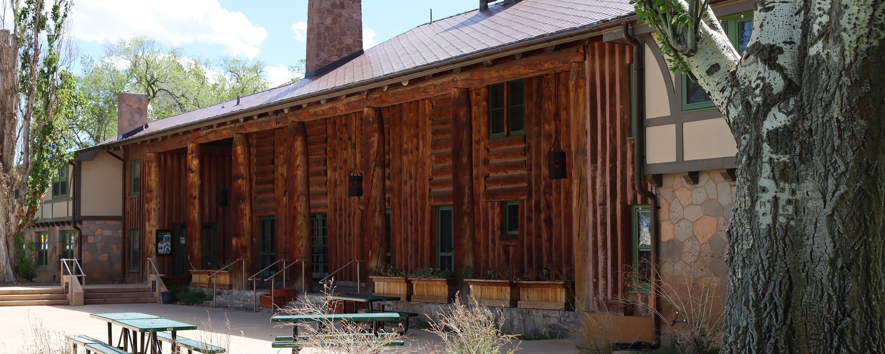 A wood log building with green framed windows and picnic tables out front.