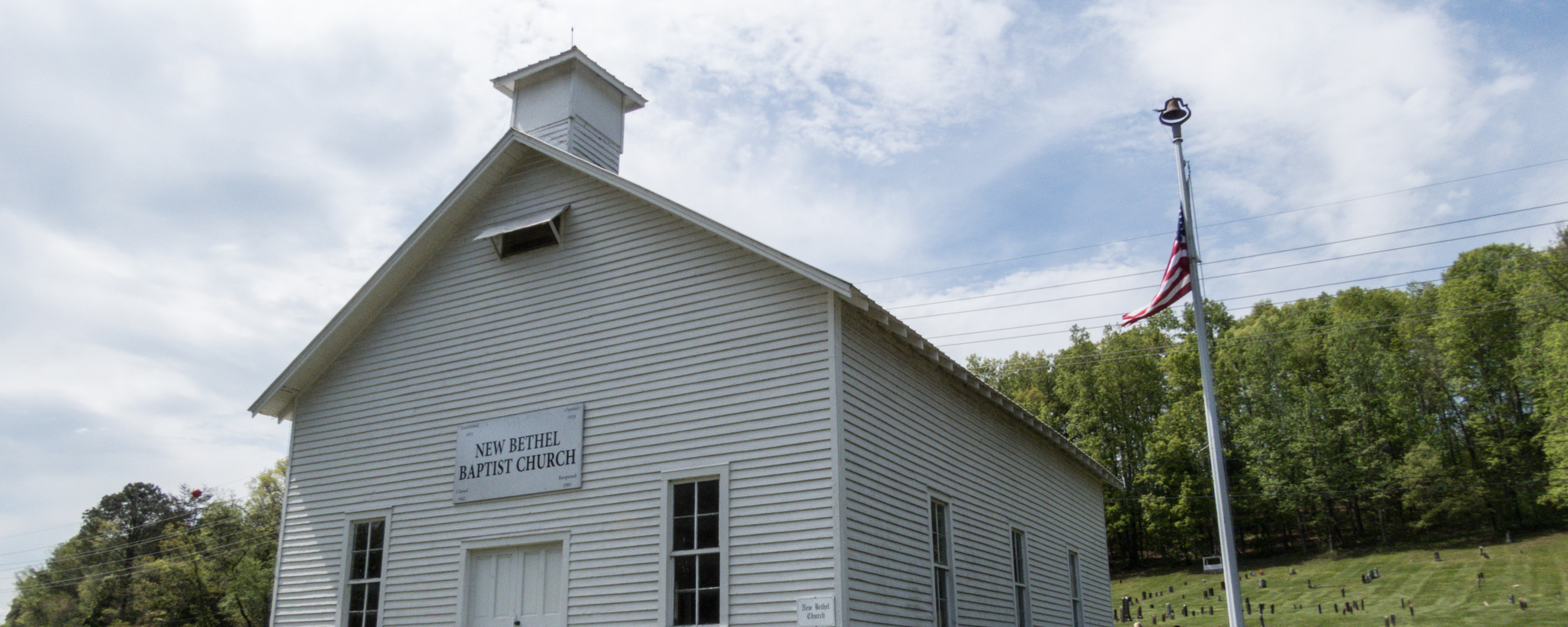The top half of a wooden white chapel with green grass and grave stones in the background.