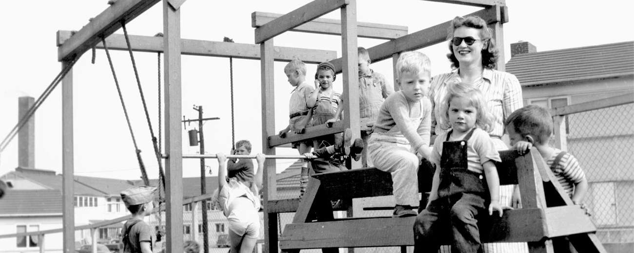 Several children are gathered atop playground equipment next to their teacher.