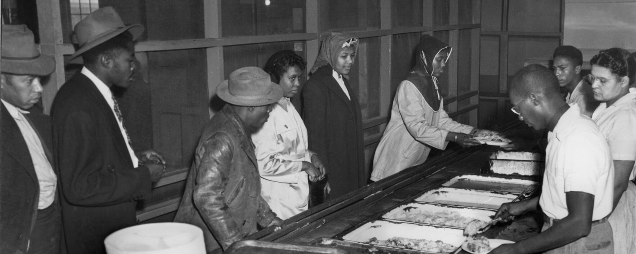 Several African American men and women being served in a cafeteria line.