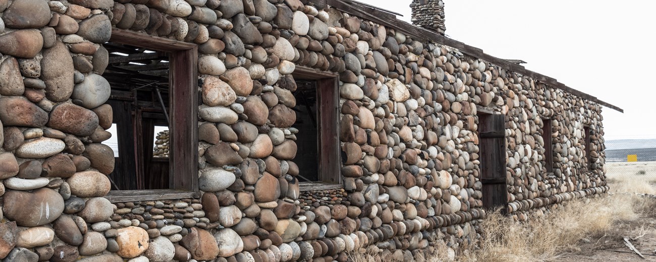 Single level cabin made of round cobblestones with wood frames for four windows and single door.