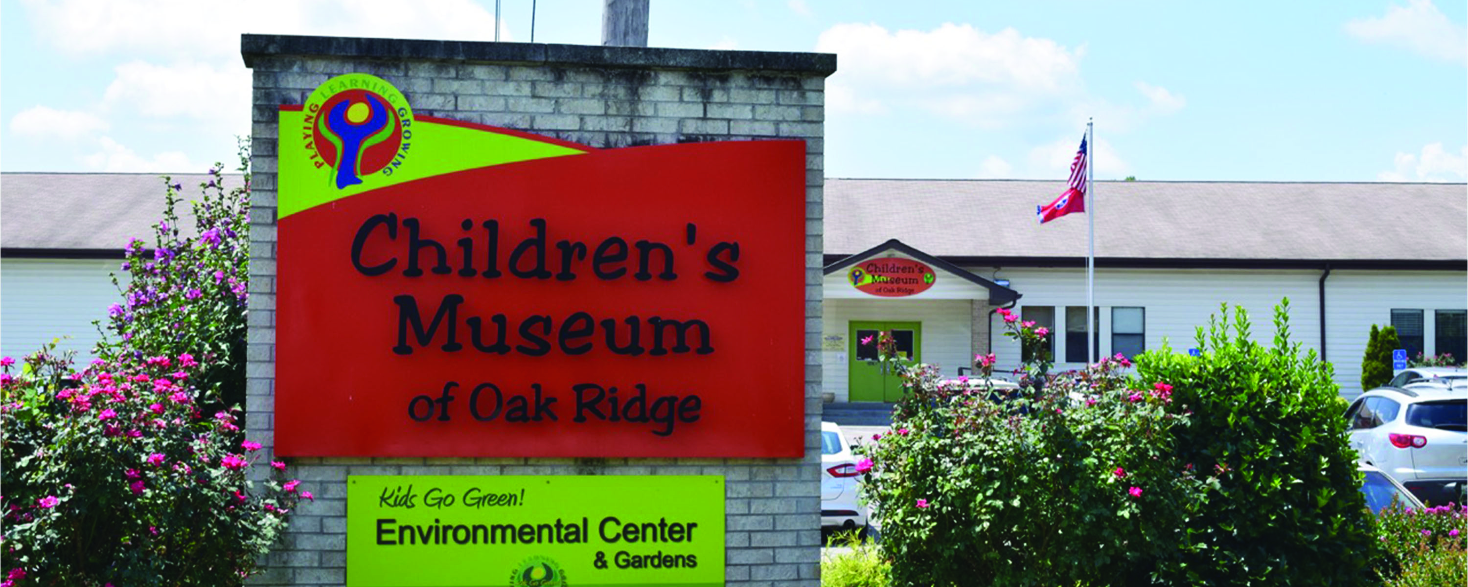 A dirty white brick sign with an orange and yellow sign that says, "Children's Museum of Oak Ridge."
