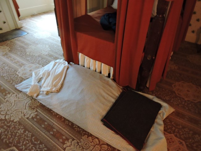 Image of a simple bedroll and pillow at the end of a four-poster bed