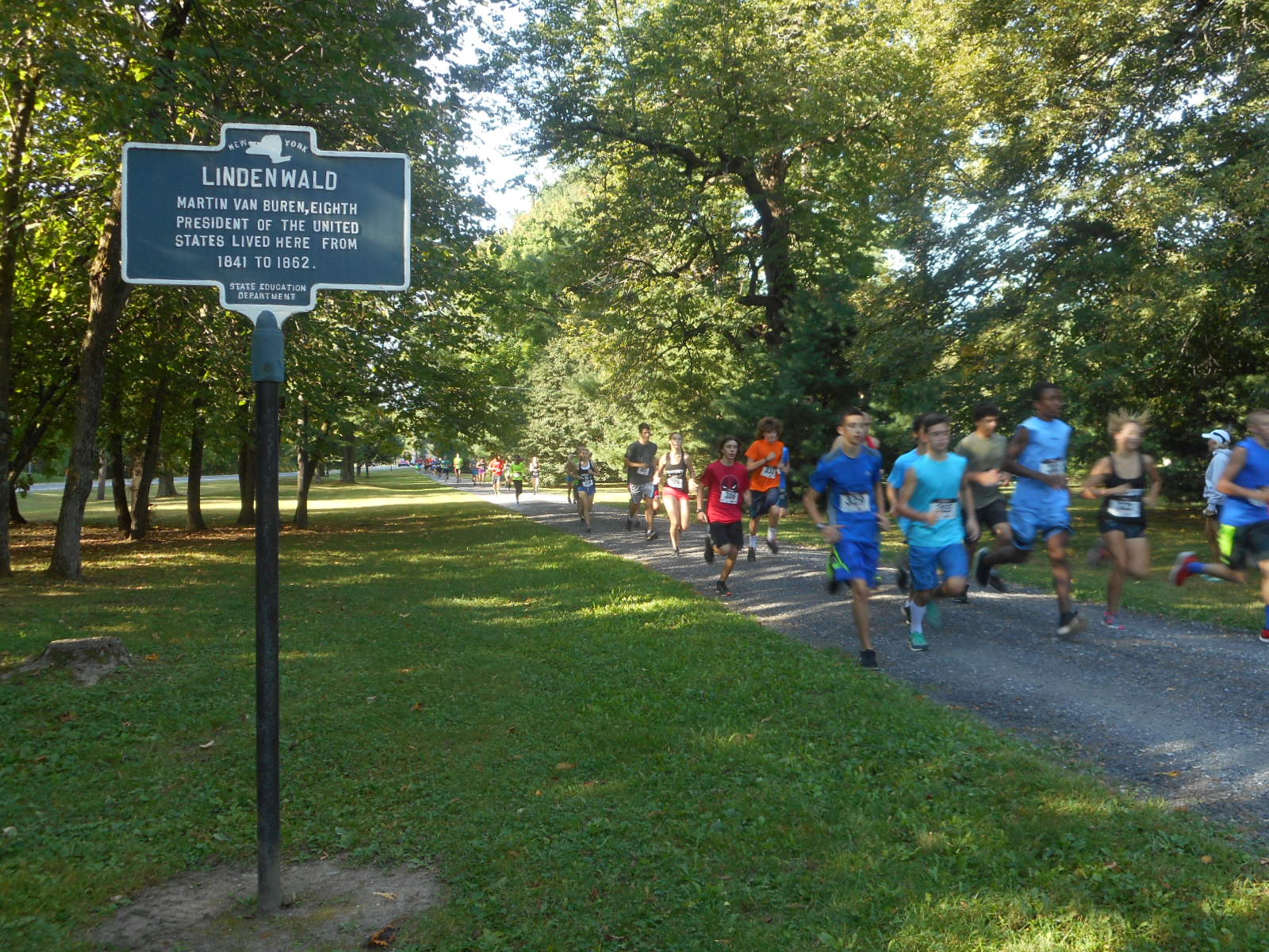Runners on a gravel road passing a sign that reads "Lindenwald"