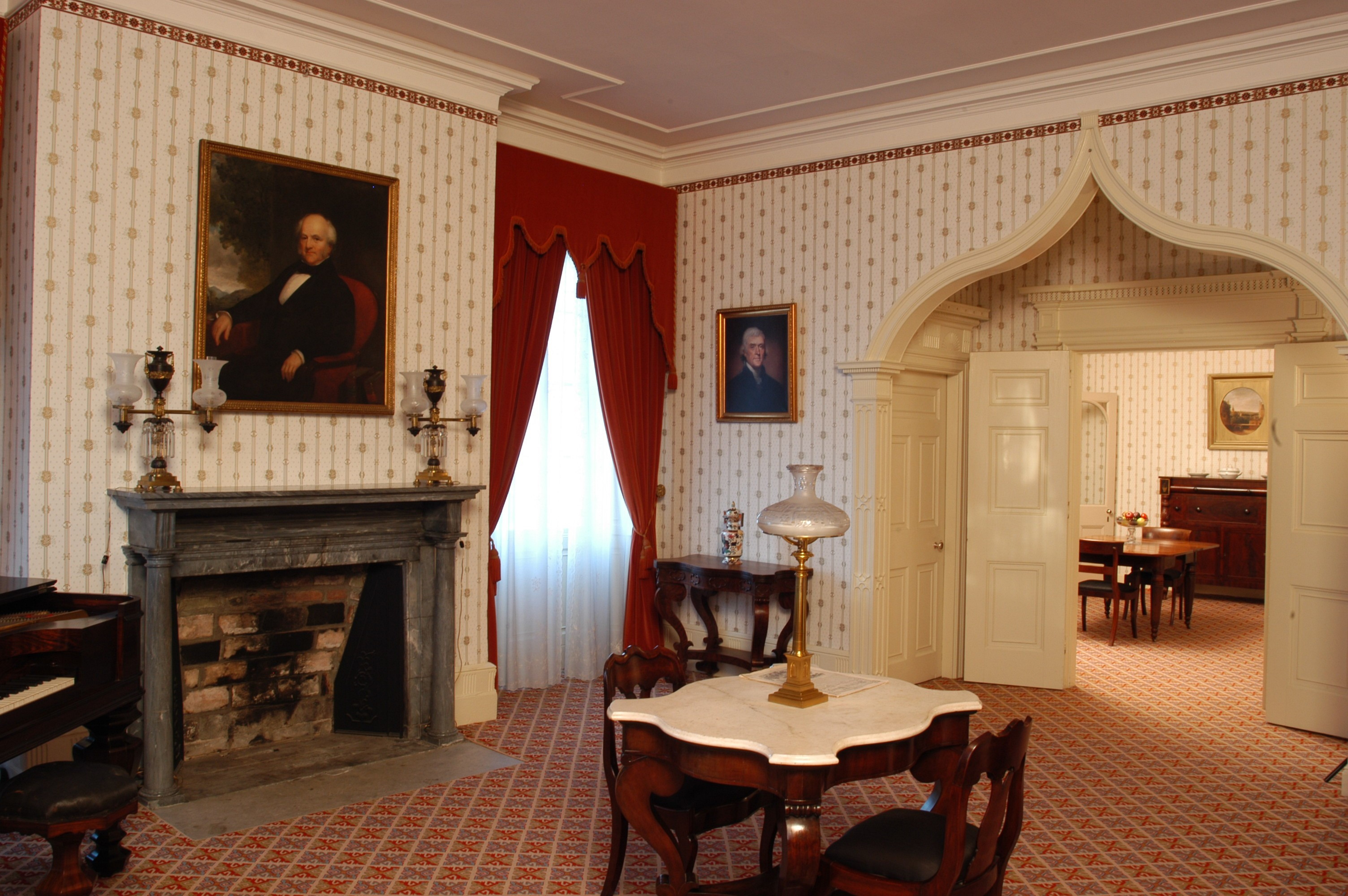 A finely decorated room with a table in the center and a portrait over the fireplace