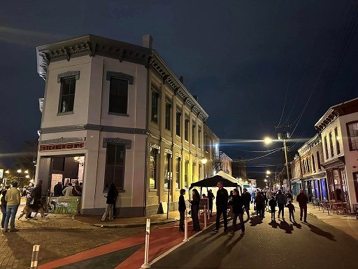 A 19th-century firehouse building lit up at night with crowds mingling outside.