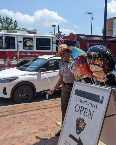 woman standing next to a sandwich board sign with balloons on it