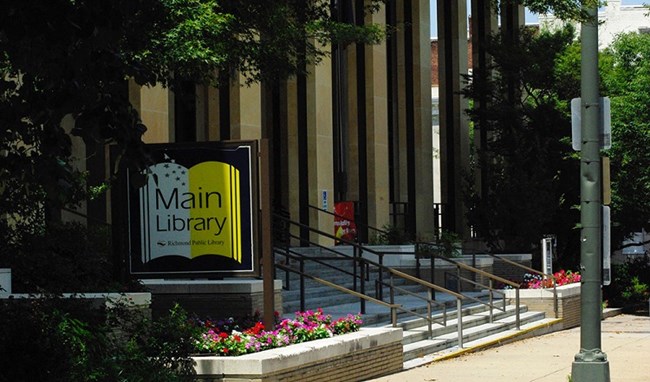 Exterior of a sidewalk and front steps of building, with a sign reading "Main Library"