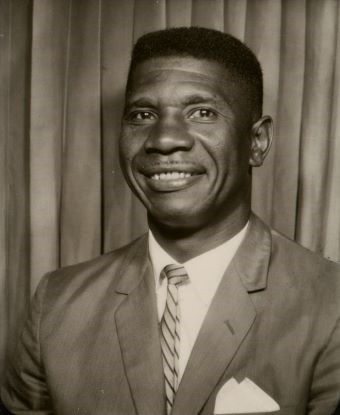 Chest up portrait of Medgar Evers in suit and tie smiling in front of drapery
