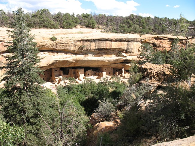 A large stonework village sits under a cracked stone alcove, surrounded by oaks and firs.