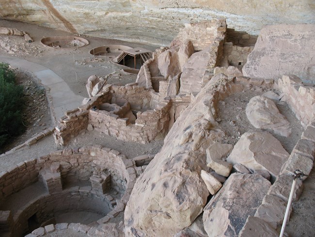 In the foreground, the remains of several stonework walls sit atop a stone ridge. Below, several pits that were the lower floor of an earlier pit house.