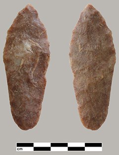 A pinkish stone shaped into a projectile point, resembling an elongated teardrop. A size guide marks the bottom of the image, showing the point is approximately 2 centimeters wide.