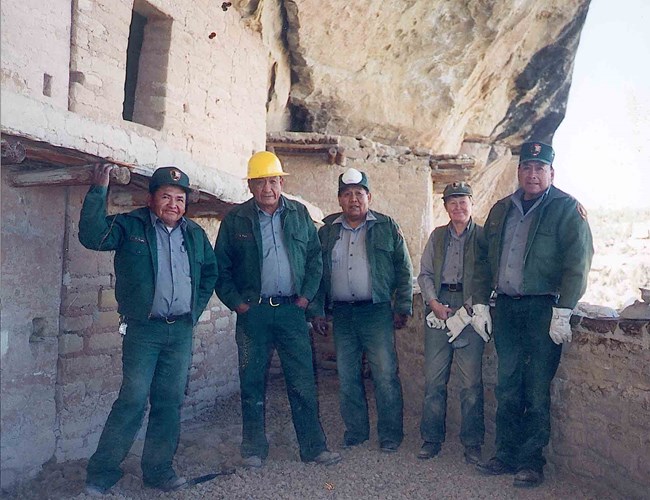 A group of five people in National Park Service uniform stand facing the camera in Balcony House, a cliffside village at Mesa Verde