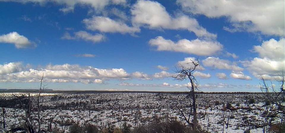 View of snowy mesa with clouded blue sky above.