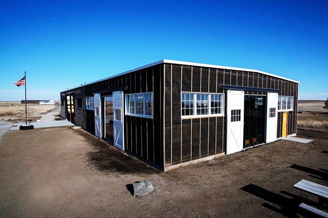 An exterior photograph of the Minidoka visitor center, a single-story structure made of wood and tar paper, repurposed from a historic warehouse.