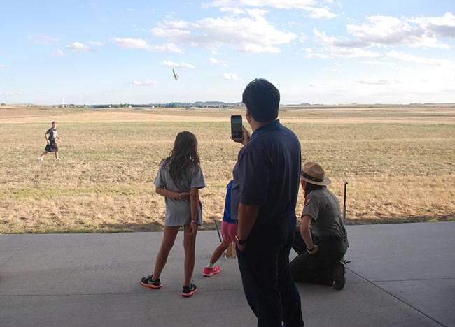 A parent takes a picture as children launch a paper rocket with a park ranger