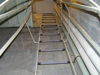 A metal ladder and safety cage go up the side of a shaft
