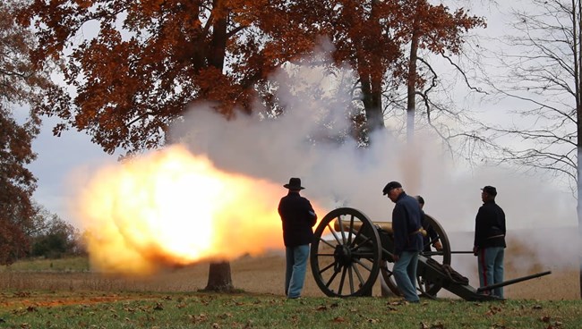 Four soldiers in blue standing around a cannon as it fires.