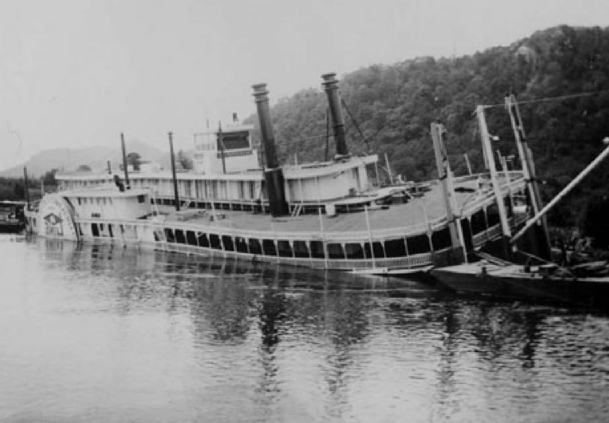 A steamboat lies sunken at the edge of the river.
