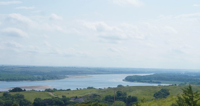 Missouri River overlook with the river bending right, green trees and grass, and sandbars in the river.