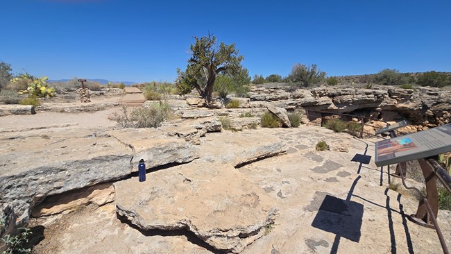 A rocky viewing area at the edge of a cliff. Several slabs of stone provide large steps down to interpretive signs. A watterbottle shows the largest steps are more than twice the height of the waterbottle. A paved trail ends in the background.
