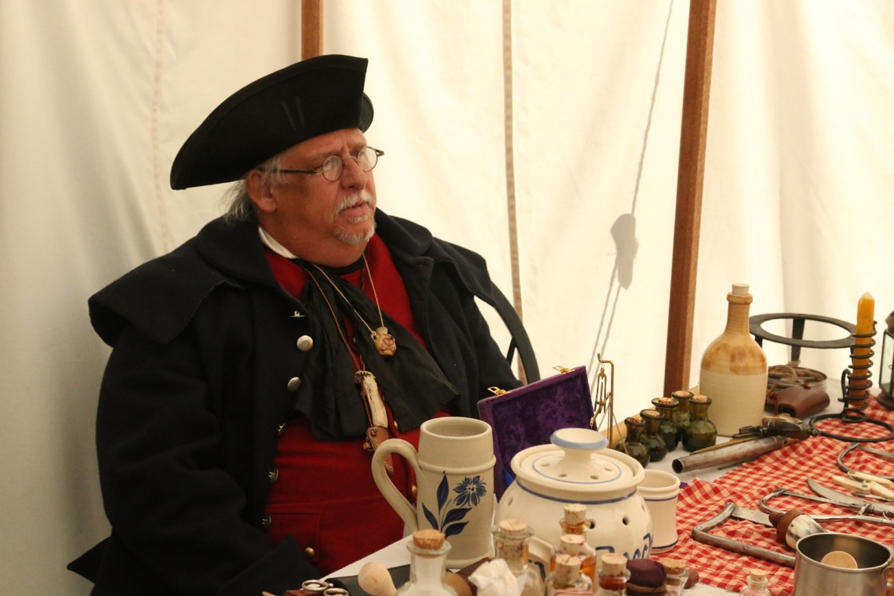 Colonial doctor sit's behind medicine table