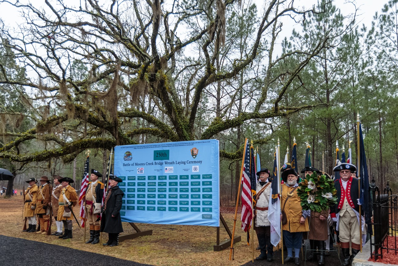 Color Guard with flags standing in front of a blue sign