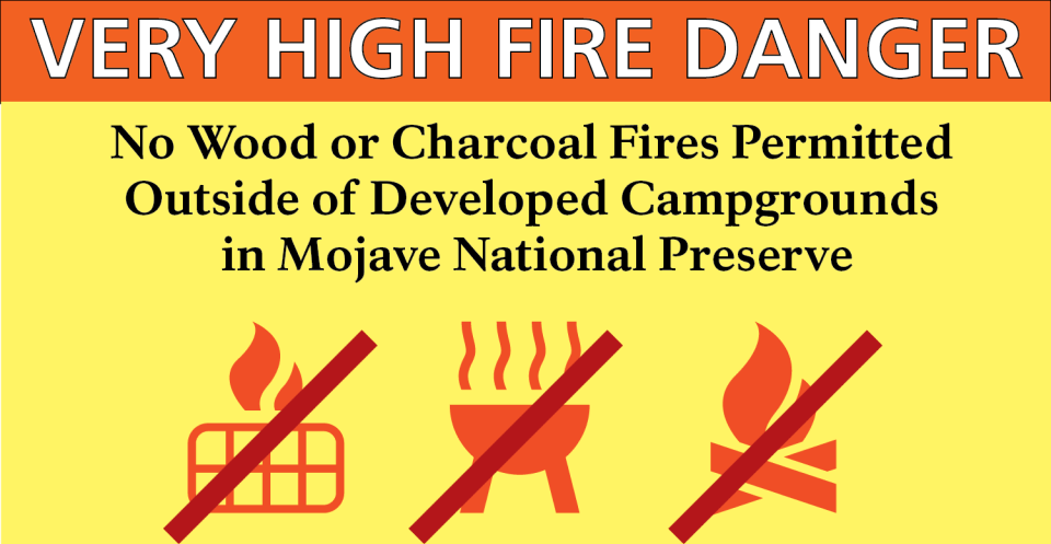Sign with title VERY HIGH FIRE DANGER and text reading No Wood or Charcoal Fires Permitted Outside of Developed Campgrounds in Mojave National Preserve lower portion of sign has icons of a grill, BBQ and campfire all with red slashes through them