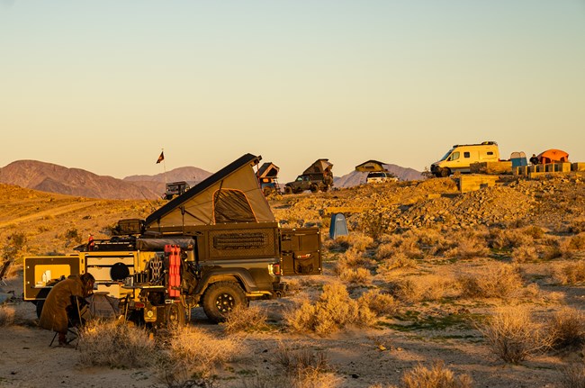 A group of off road four wheel drive vehicles with rooftop tents in sunset light of a desert landscape