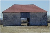 A stone barn with a red hipped roof.