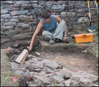 A worker clears dirt from a row of stones in an archeology dig.