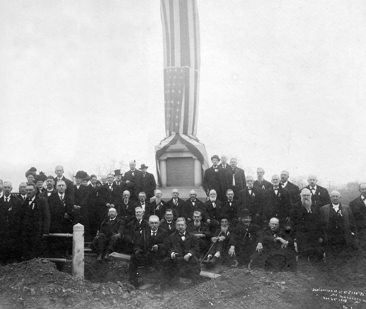 A group of elderly Civil War veterans sit in front of a tall monument shrouded in the American flag.