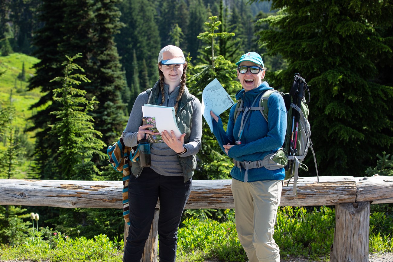 Two female volunteers pose on the trail with maps to hand out to visitors.
