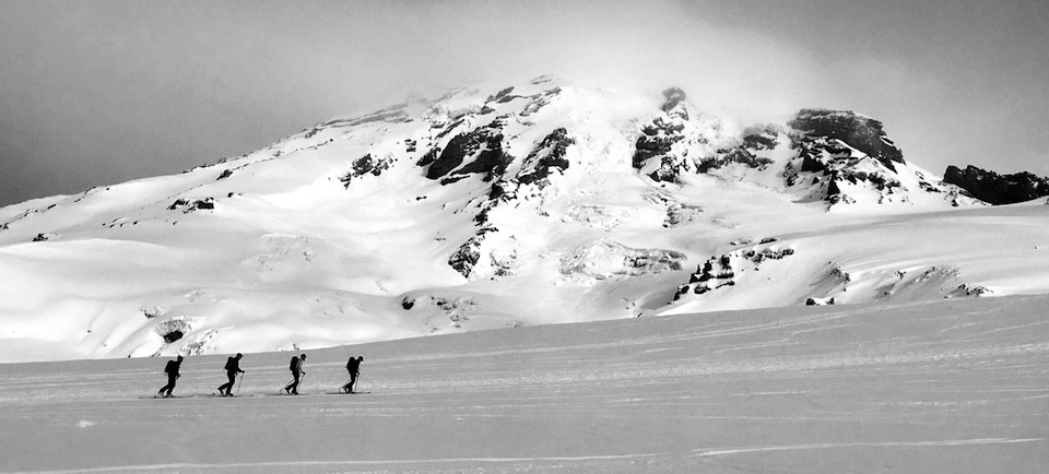 Four skiers cross a snowy slope on the side of Mount Rainier.