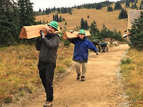 Two volunteers carrying log sections down a trail.
