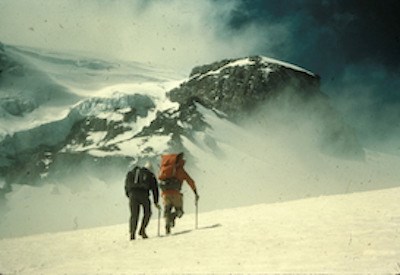 Two people walking across a snow slope with full packs