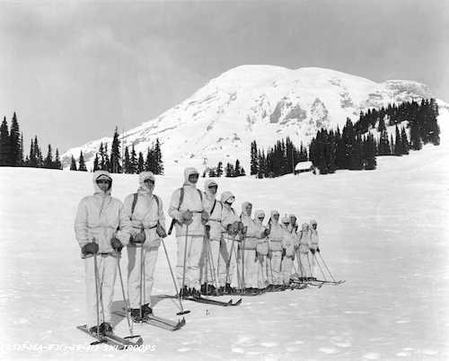 A dozen men in white uniforms on the snow with skis.